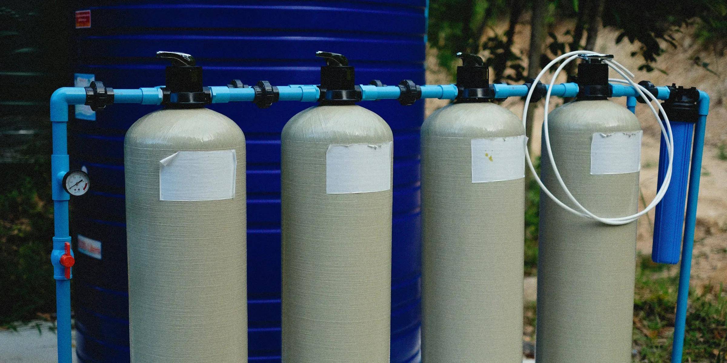 A row of fiberglass mineral tanks with control valves on top, plumbed together with blue pipe